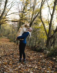 Services 1 A woman joyfully embraces her dog on a foliage-covered forest trail in autumn.