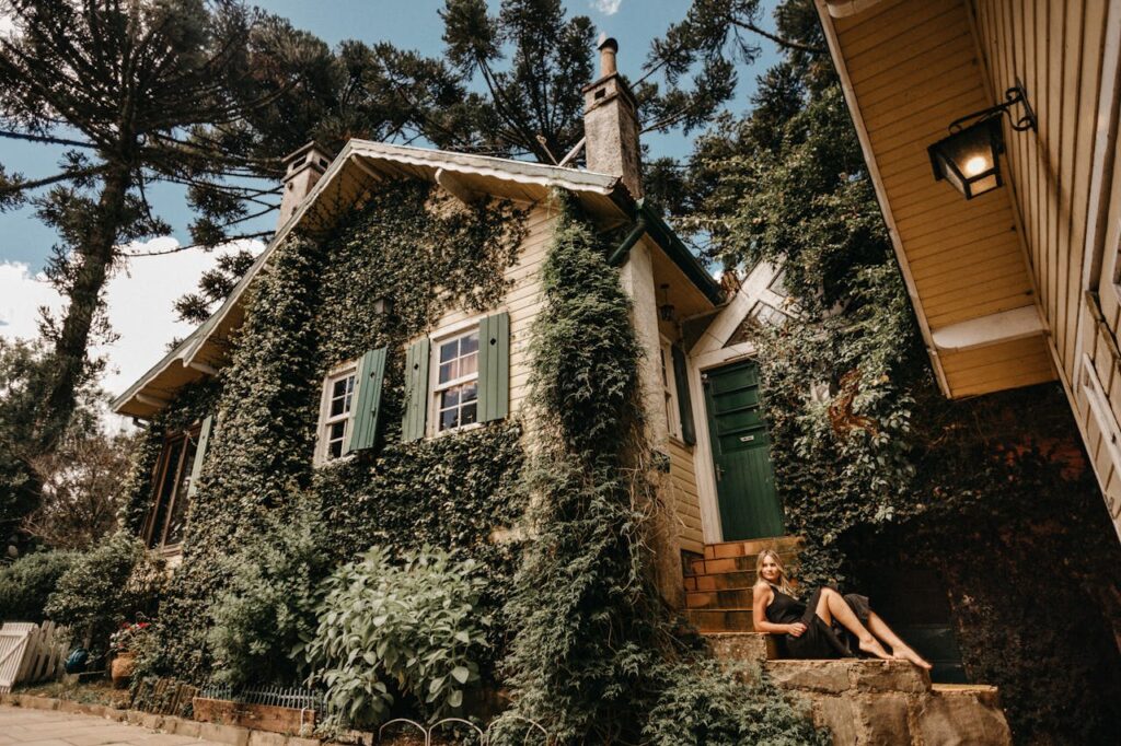 Services 4 A woman sitting on a staircase by a charming ivy-covered cottage surrounded by greenery.
