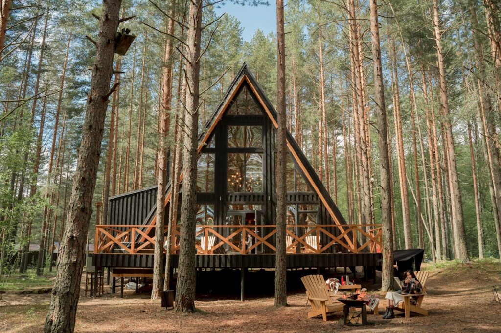 pexels-photo-9211816 A-frame cabin nestled among pine trees with outdoor seating, perfect for relaxation and nature getaways.